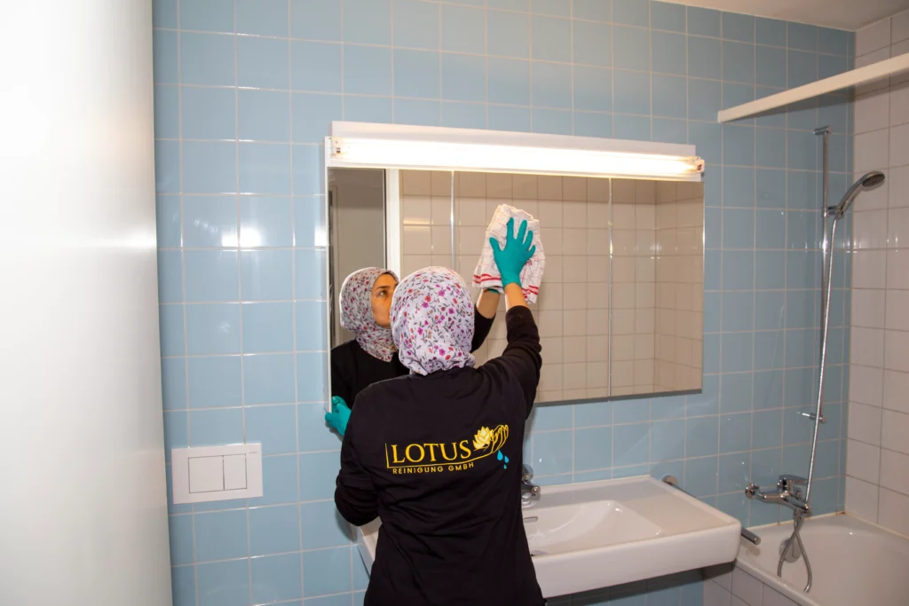 Person reinigt Badezimmerspiegel mit Tuch und Handschuhen
