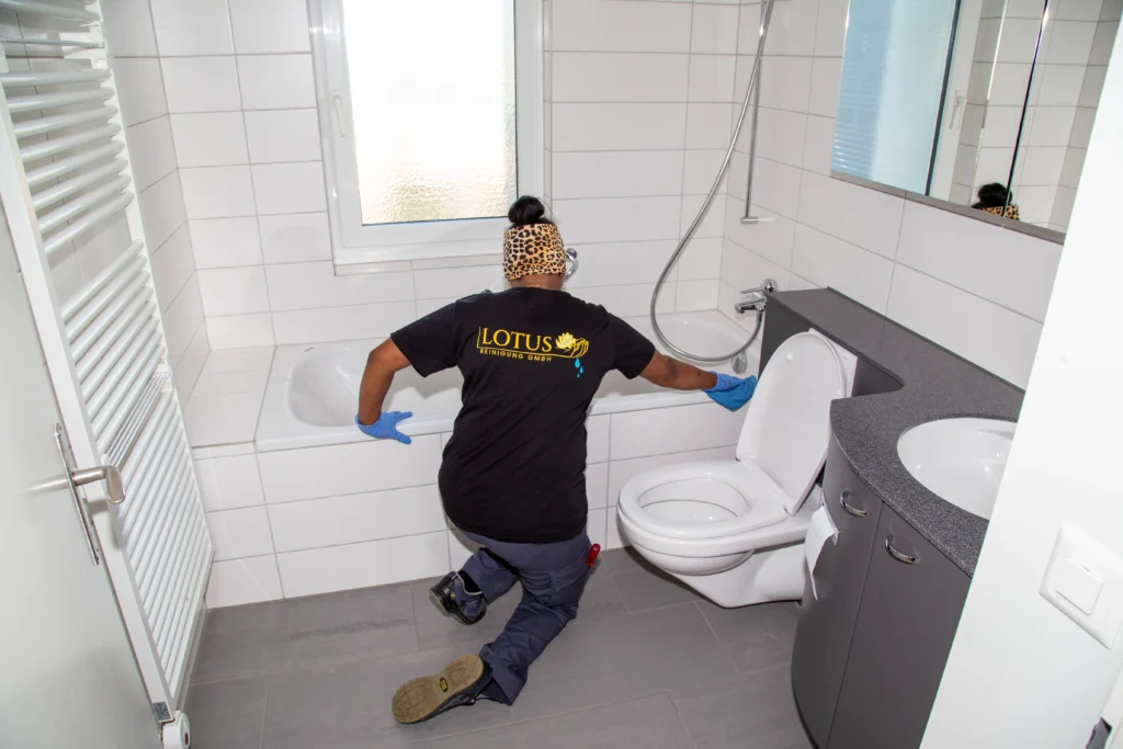 Reinigungskraft putzt Badezimmer mit Schutzbekleidung.